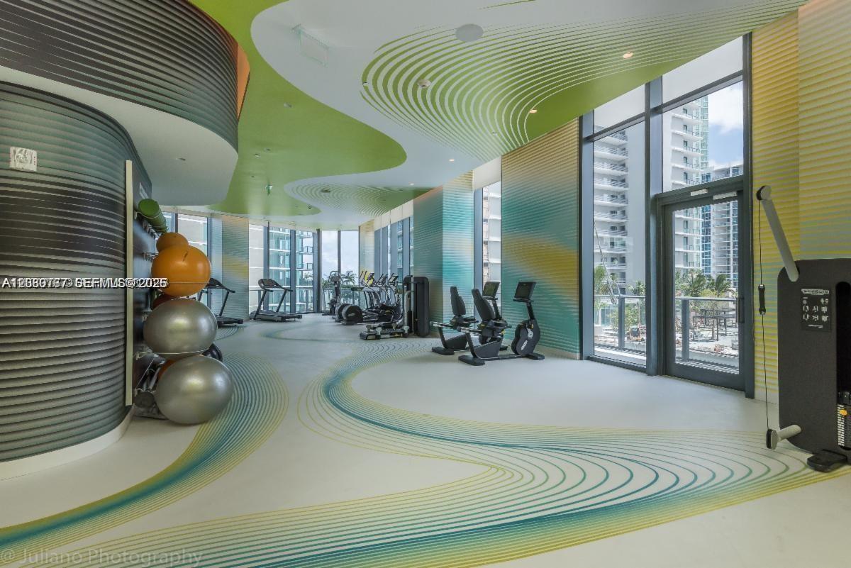 A modern gym features curved walls, patterned flooring, and floor-to-ceiling windows overlooking a city — MIAMI, FL
