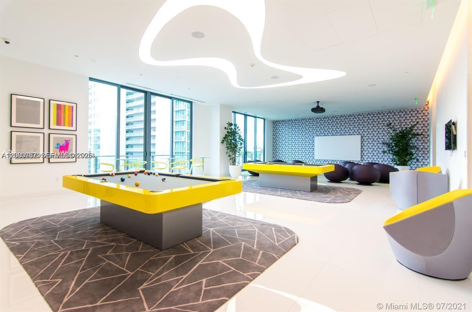 A modern game room features two yellow pool tables, geometric rugs, and floor-to-ceiling windows — MIAMI, FL