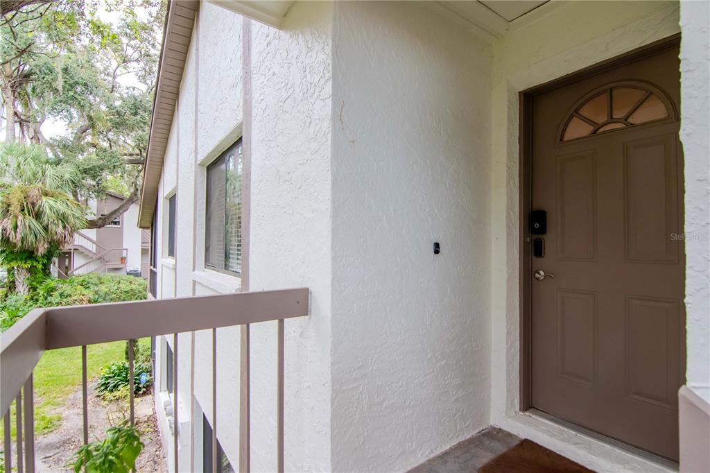 A brown front door with a small window sits on a white stucco exterior balcony — 2363 FLANDERS WAY UNIT C, SAFETY HARBOR, FL