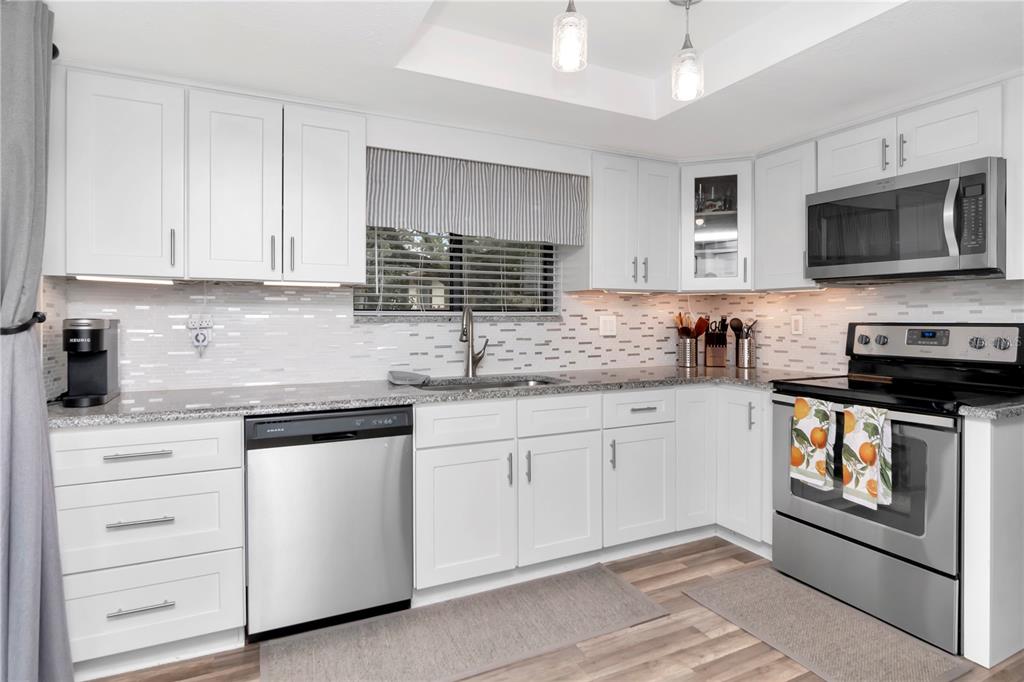 A kitchen with white cabinets, stainless steel appliances, granite countertops, and a tiled backsplash — 2363 FLANDERS WAY UNIT C, SAFETY HARBOR, FL