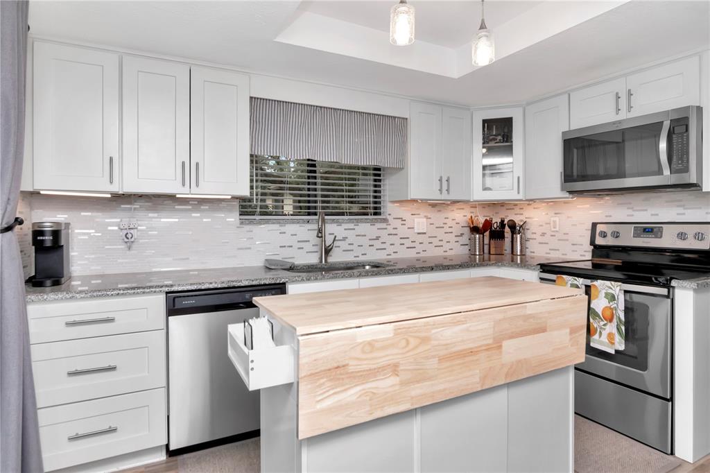 A kitchen features white cabinets, stainless steel appliances, a granite countertop, and a wooden island — 2363 FLANDERS WAY UNIT C, SAFETY HARBOR, FL