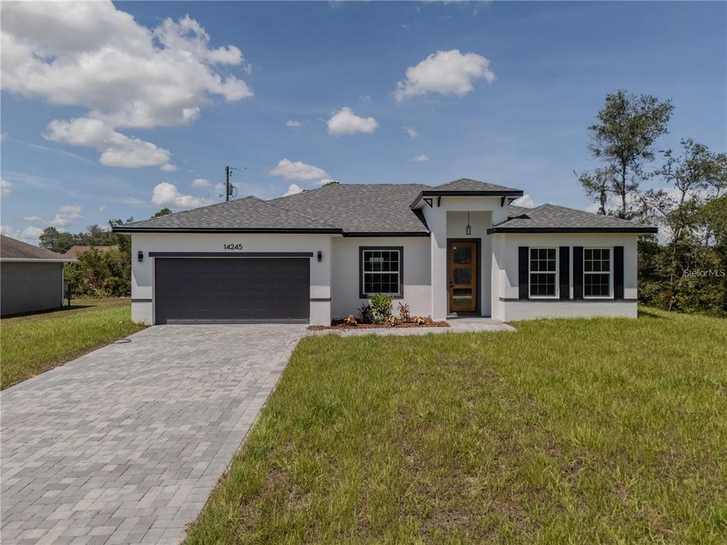 A single-story house with a white stucco exterior, dark garage door, and gray shingled roof — 14245 SW 28TH COURT, OCALA, FL