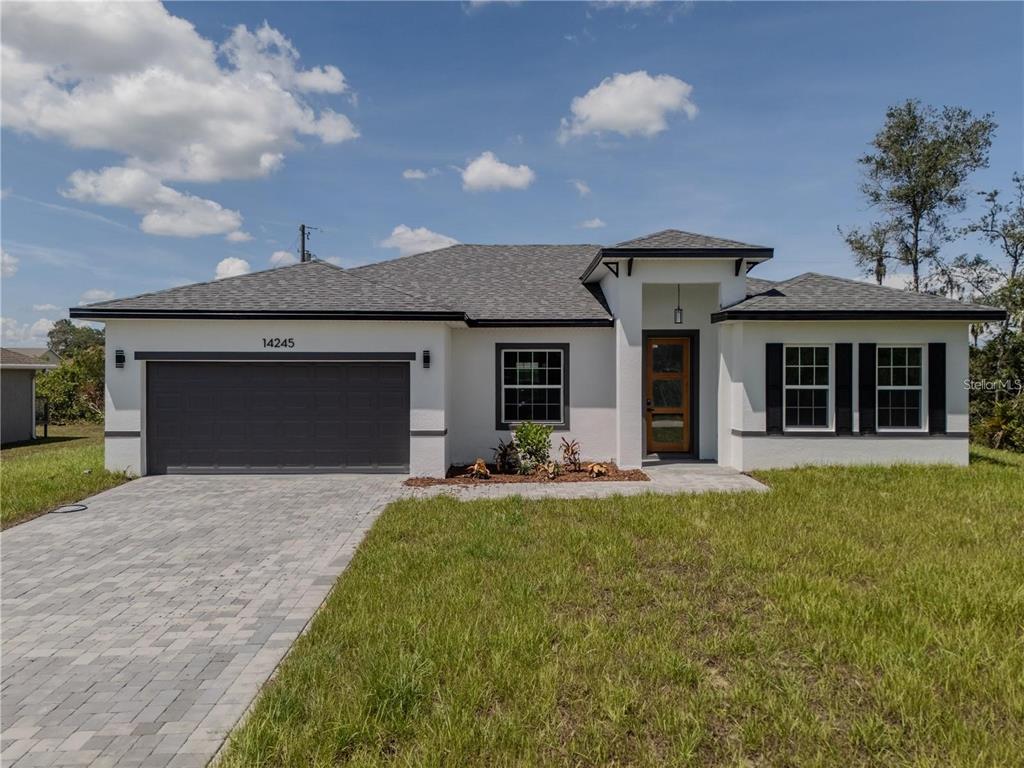 A single-story house with white stucco walls, a dark garage door, and a paved driveway — 14245 SW 28TH COURT, OCALA, FL