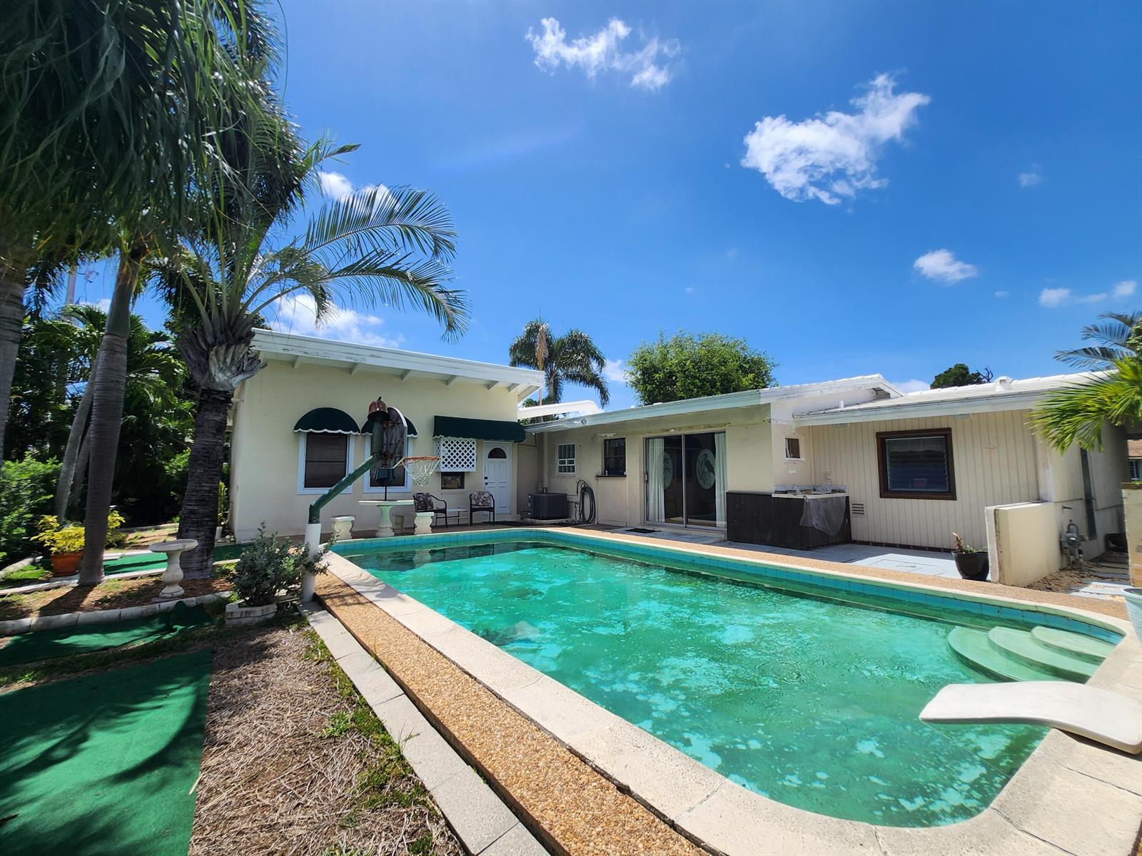 A swimming pool sits in the backyard of a single-story house with palm trees — 111 SE 7th Street, Pompano Beach FL 33060, POMPANO BEACH, FL