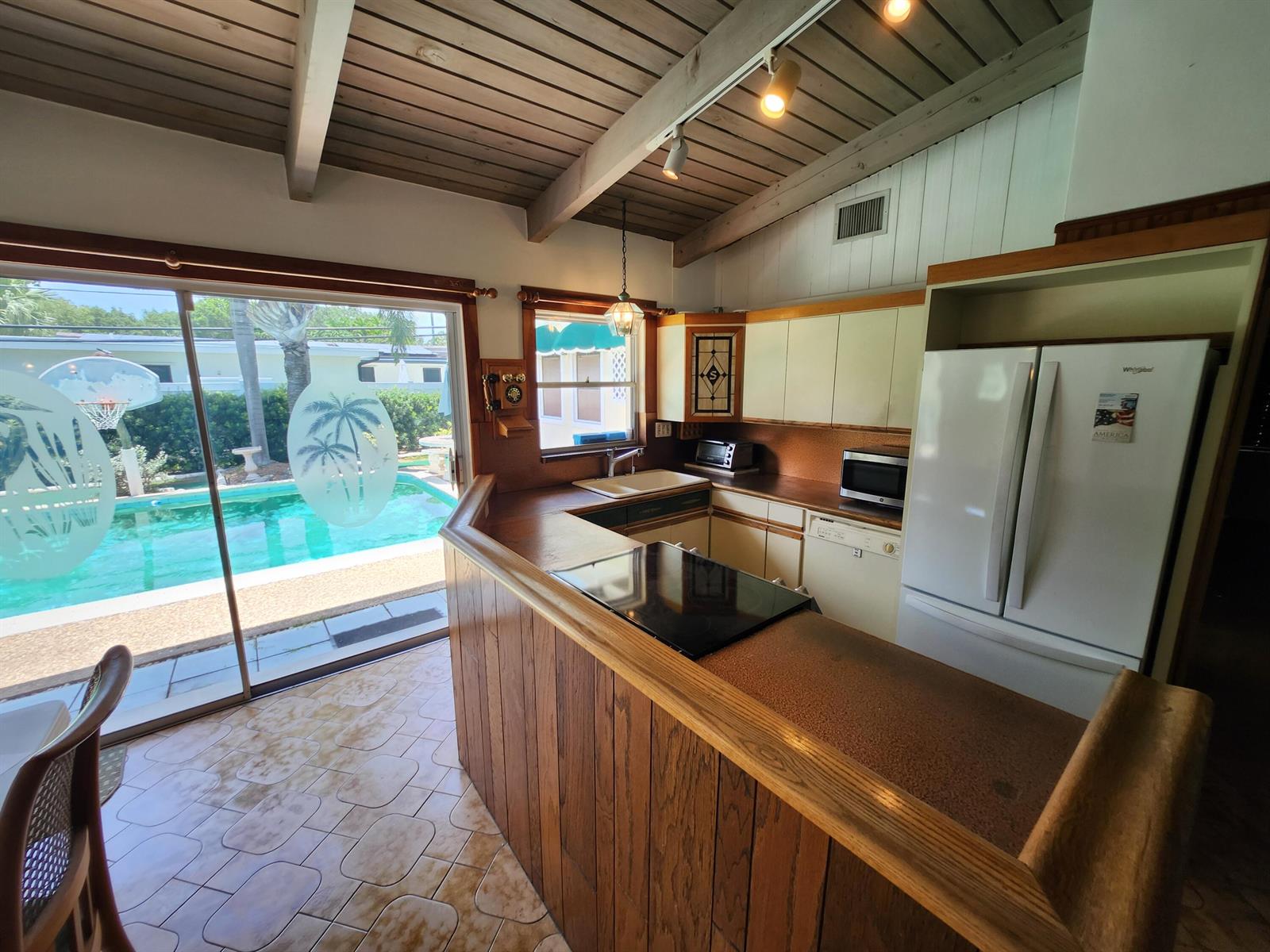 A kitchen with wood paneling, white cabinets, and a sliding door overlooking a swimming pool — 111 SE 7th Street, Pompano Beach FL 33060, POMPANO BEACH, FL