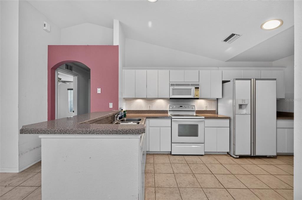 A kitchen with white cabinets, white appliances, a speckled countertop, and a pink arched wall — 19735 SW 93RD PLACE, DUNNELLON, FL