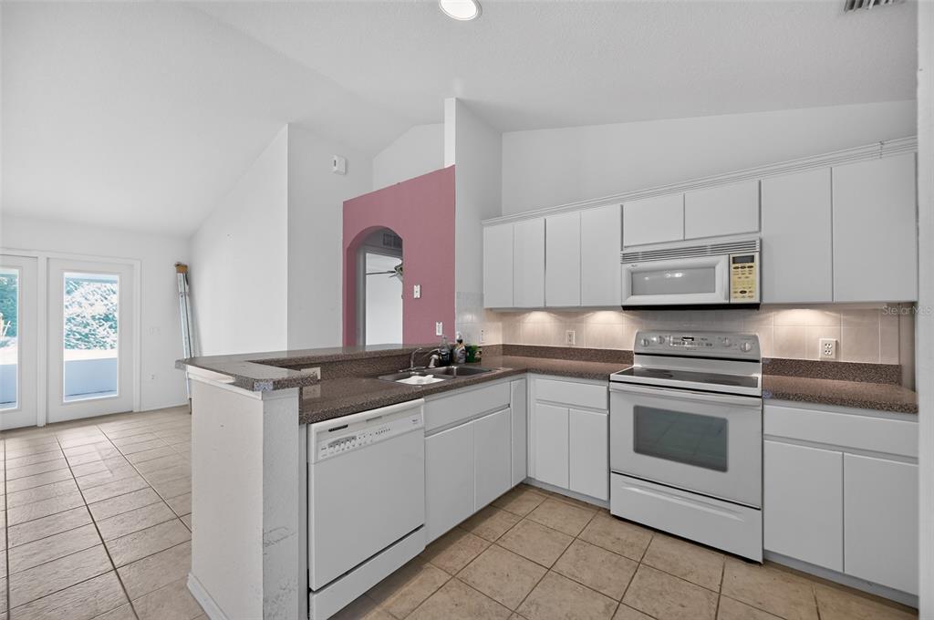 A kitchen with white cabinets, granite countertops, and tile flooring, featuring a breakfast bar — 19735 SW 93RD PLACE, DUNNELLON, FL