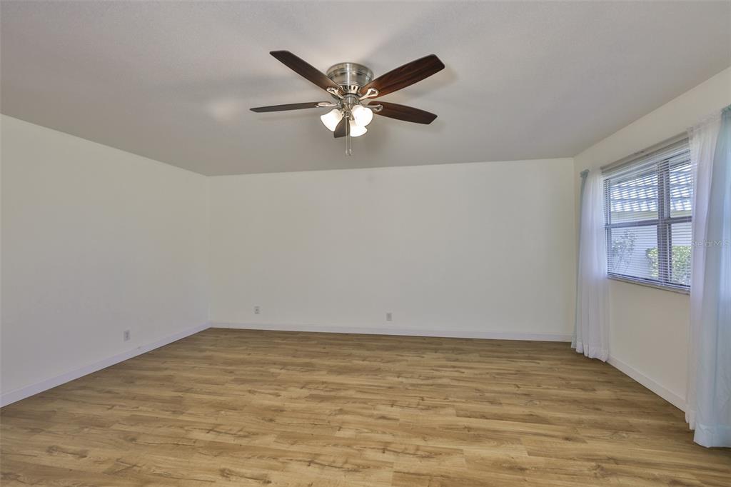 An empty room with light wood-look flooring, white walls, a ceiling fan, and a window — 1811 BEDFORD LANE UNIT 153, SUN CITY CENTER, FL