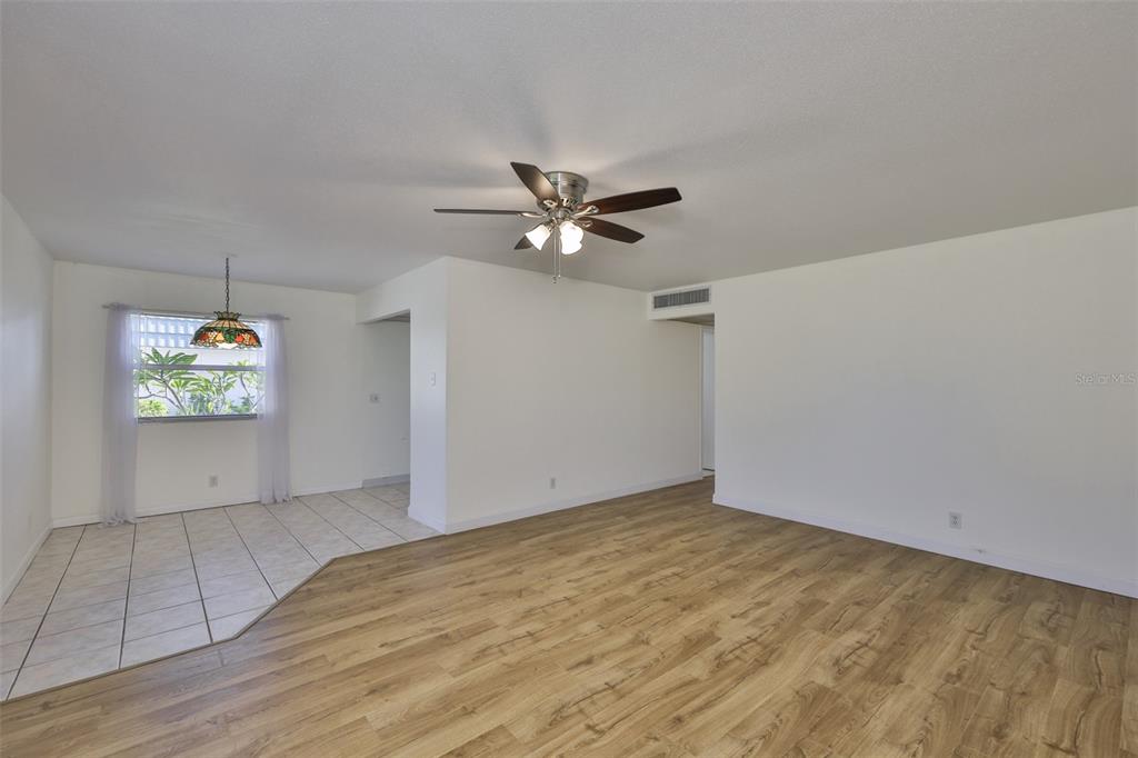 A room with wood-look flooring, a ceiling fan, and a tiled dining area with window — 1811 BEDFORD LANE UNIT 153, SUN CITY CENTER, FL