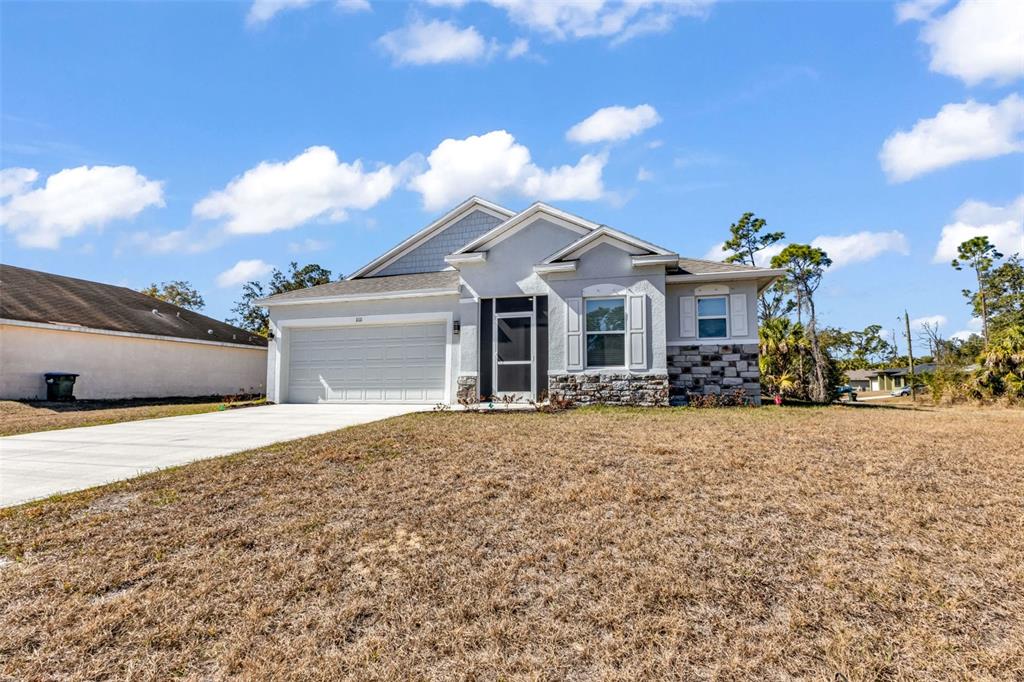 A single-story house with a white garage, stone accents, and a dry grass lawn — 1111 S MCDUFF STREET, NORTH PORT, FL