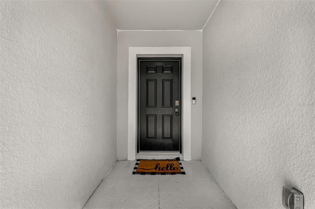 A black front door with a white frame sits at the end of a covered entryway — 1111 S MCDUFF STREET, NORTH PORT, FL