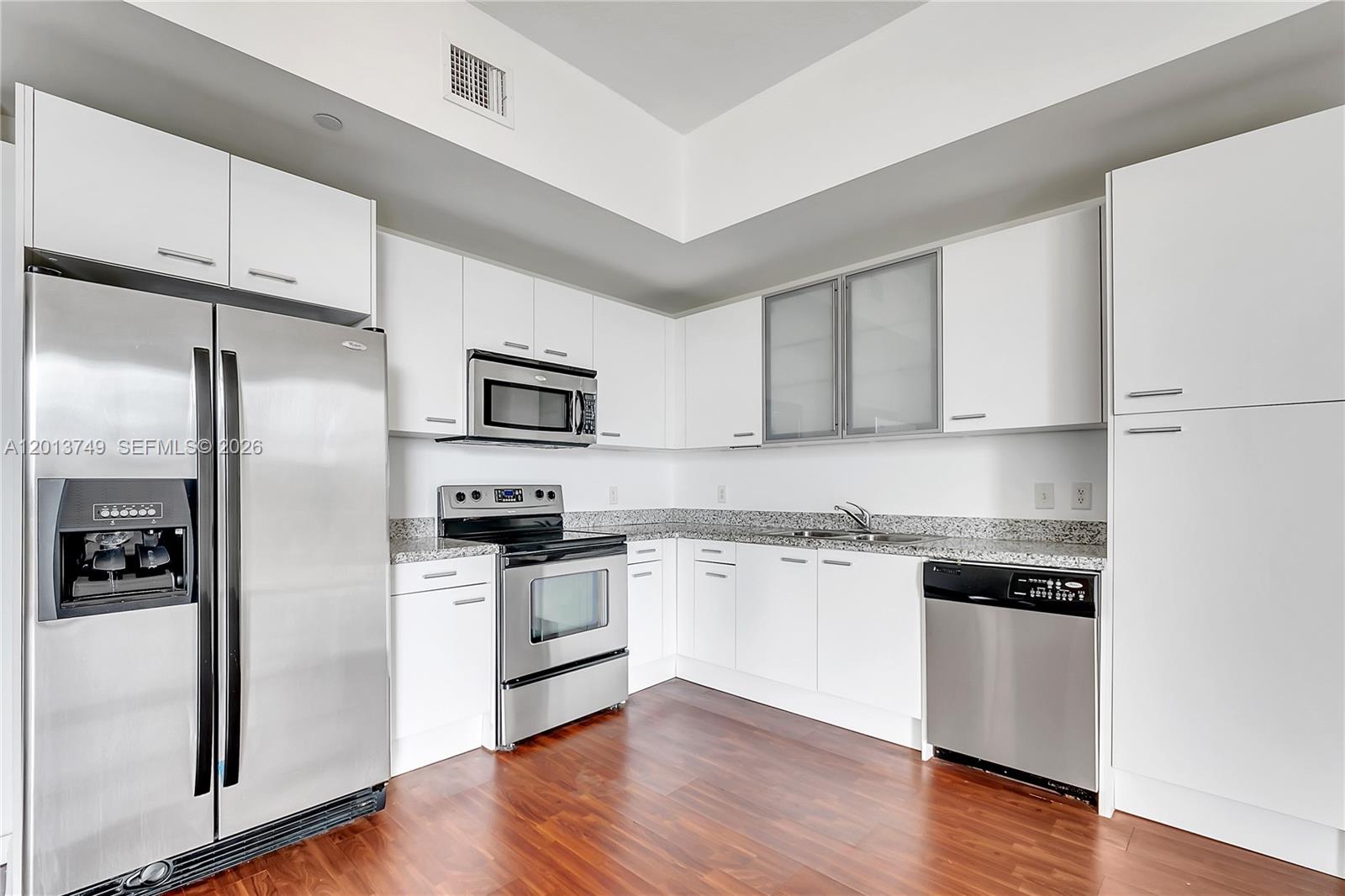 A kitchen features white cabinets, stainless steel appliances, granite countertops, and dark wood flooring — 1350 NW 8th Ct # 4, Miami FL 33136, MIAMI, FL