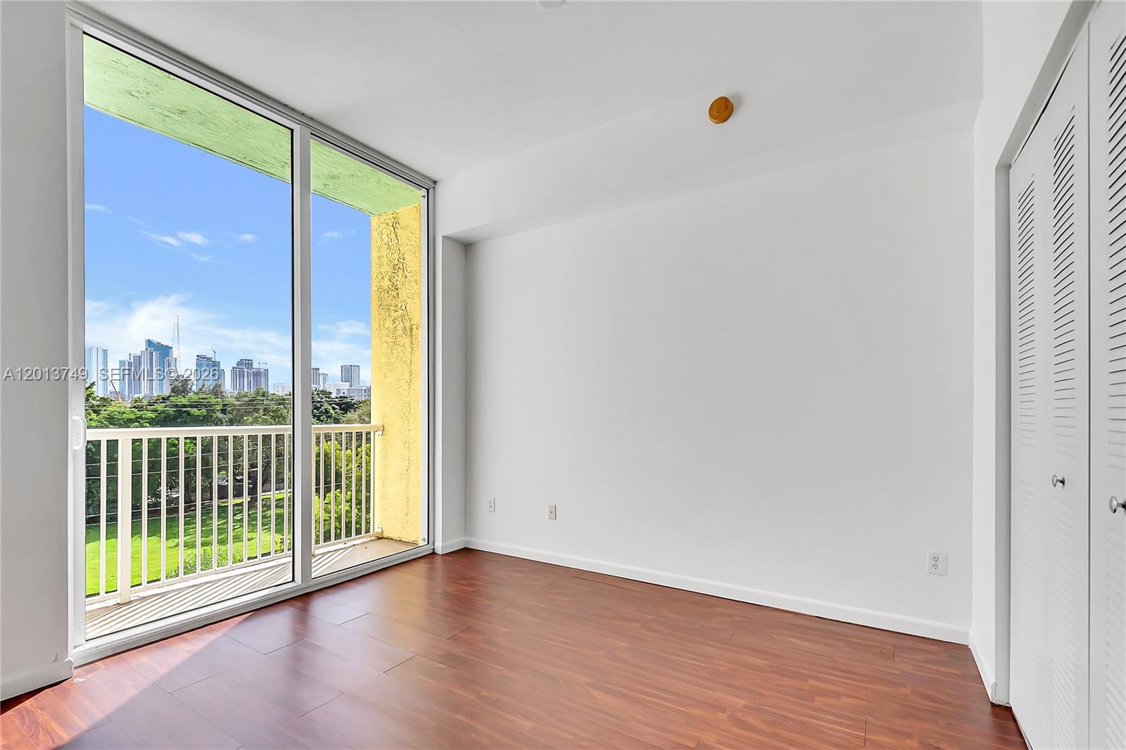 An empty room features dark wood-look flooring, white walls, a sliding glass door, and a balcony — 1350 NW 8th Ct # 4, Miami FL 33136, MIAMI, FL