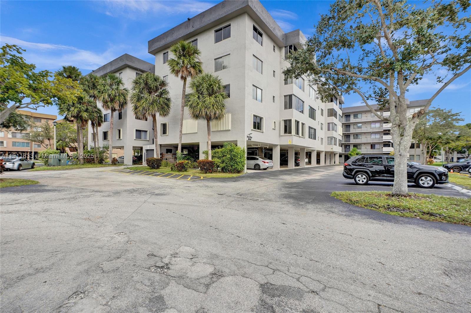 A multi-story apartment building with covered ground-level parking and palm trees in the foreground — 8010 Hampton Blvd # 211, North Lauderdale FL 33068, NORTH LAUDERDALE, FL