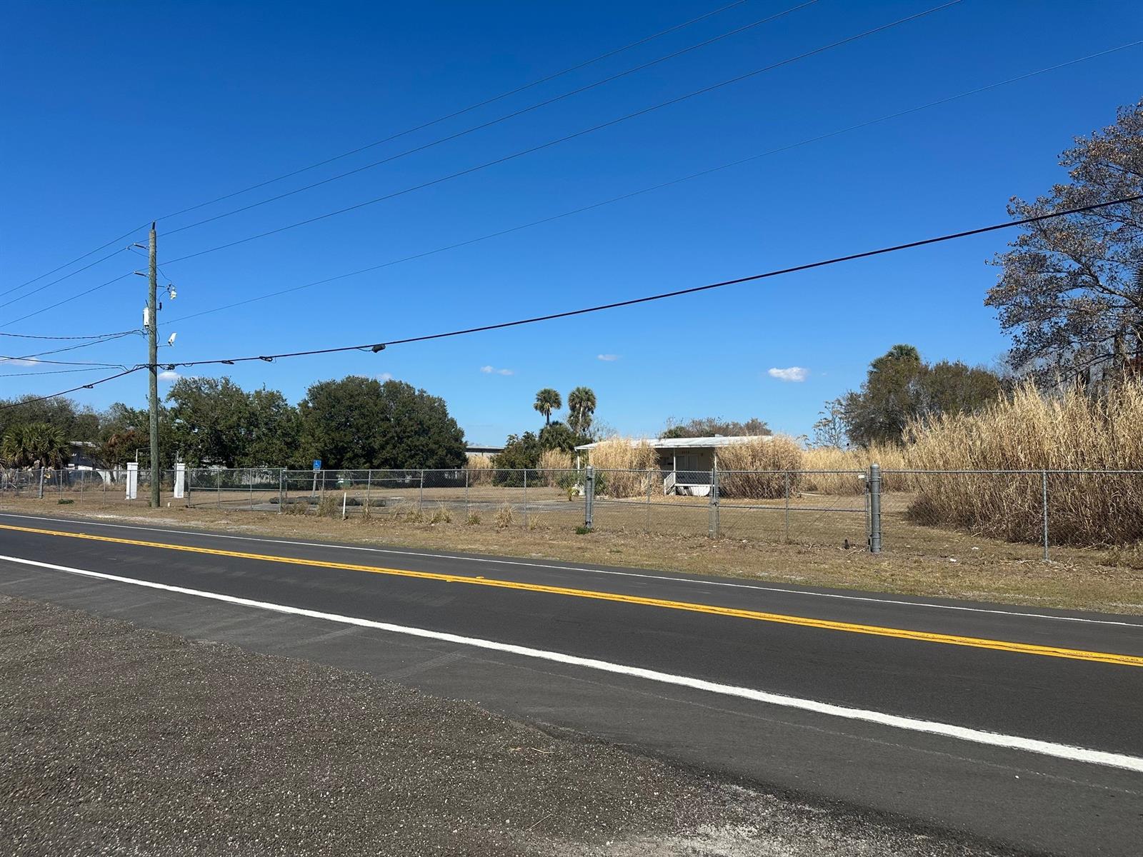 A fenced, vacant lot with tall grass and a small structure sits beside a road — 5335 HWY 441 SE, FL 34974, FL