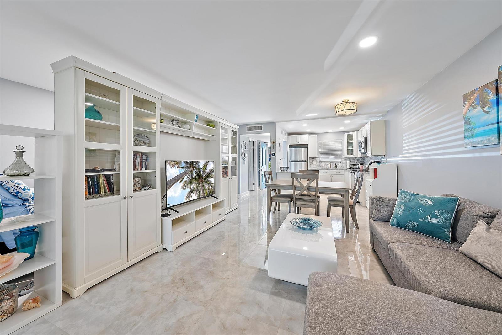 An open-concept living and dining area features white cabinetry, tile flooring, and a gray sofa — 725 Lori Drive # 111, Palm Springs FL 33461, PALM SPRINGS, FL