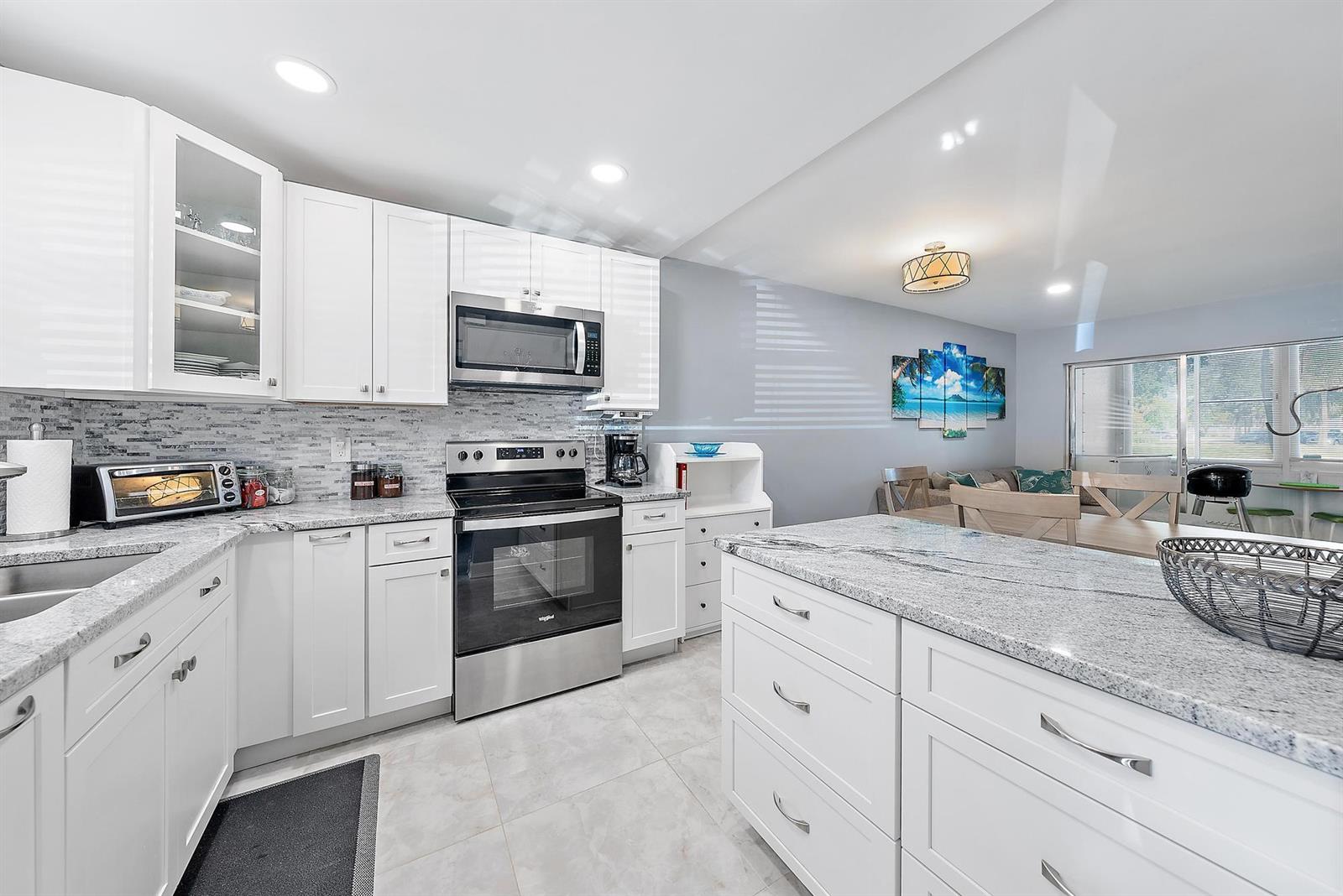 A modern kitchen features white cabinets, granite countertops, stainless steel appliances, and tile flooring — 725 Lori Drive # 111, Palm Springs FL 33461, PALM SPRINGS, FL