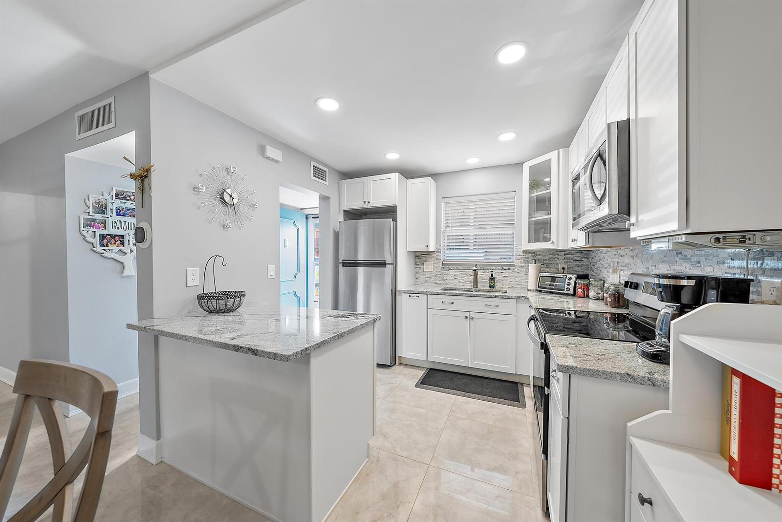 A modern kitchen features white cabinets, granite countertops, stainless steel appliances, and tile flooring — 725 Lori Drive # 111, Palm Springs FL 33461, PALM SPRINGS, FL
