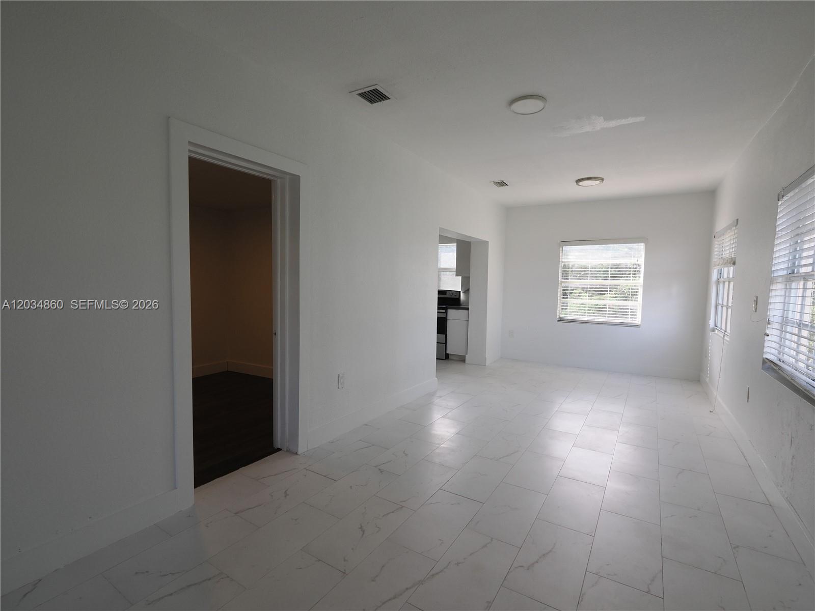 A bright room features white marble-look tile flooring, white walls, and a view into a kitchen — 2272 NW 2nd St # 2, Miami FL 33125, MIAMI, FL