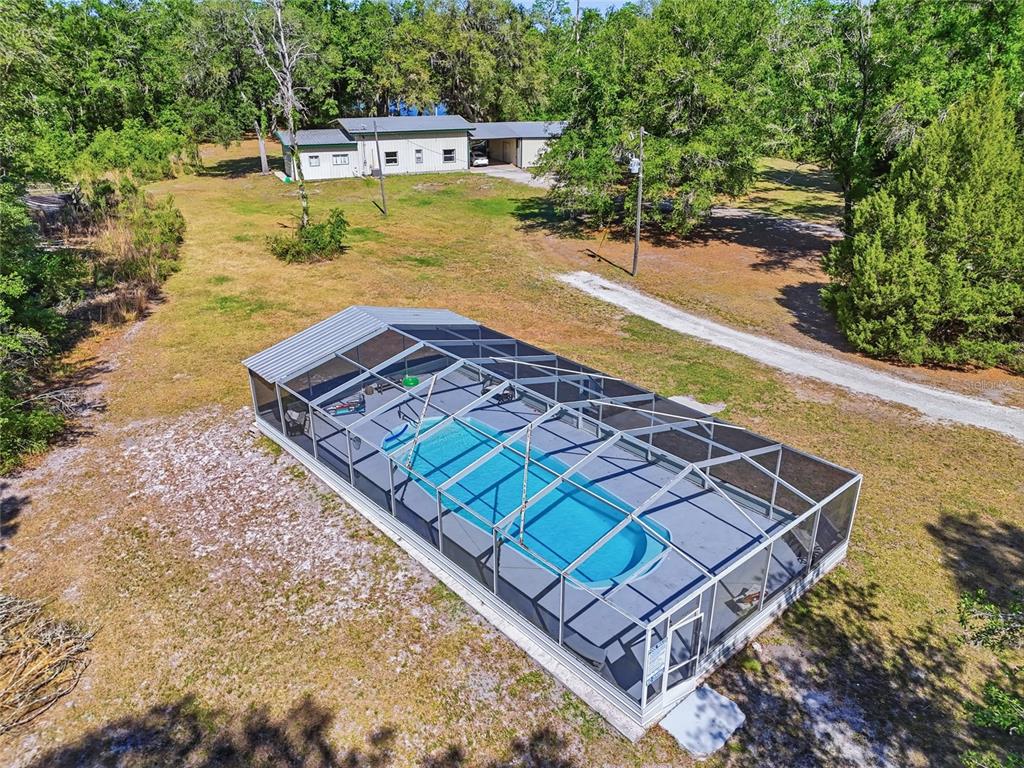 An aerial view shows a screened-in swimming pool in a large, grassy, wooded yard — 401 SE FALCON ROAD, BRANFORD, FL