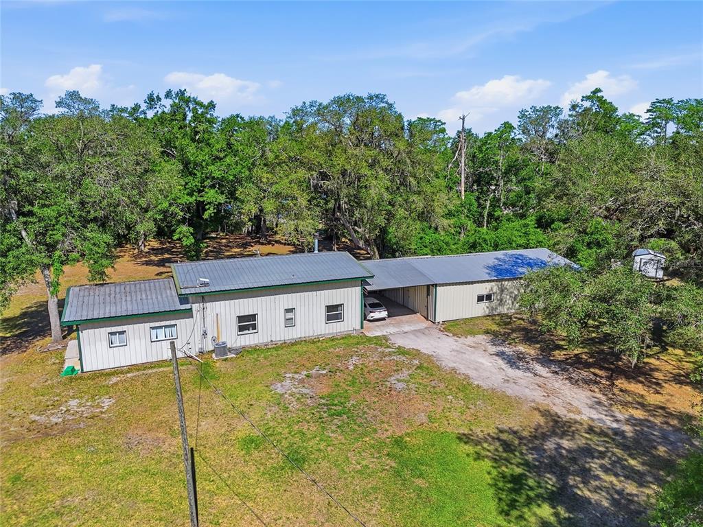 An aerial view shows a metal-roofed house with a carport and surrounding wooded yard — 401 SE FALCON ROAD, BRANFORD, FL