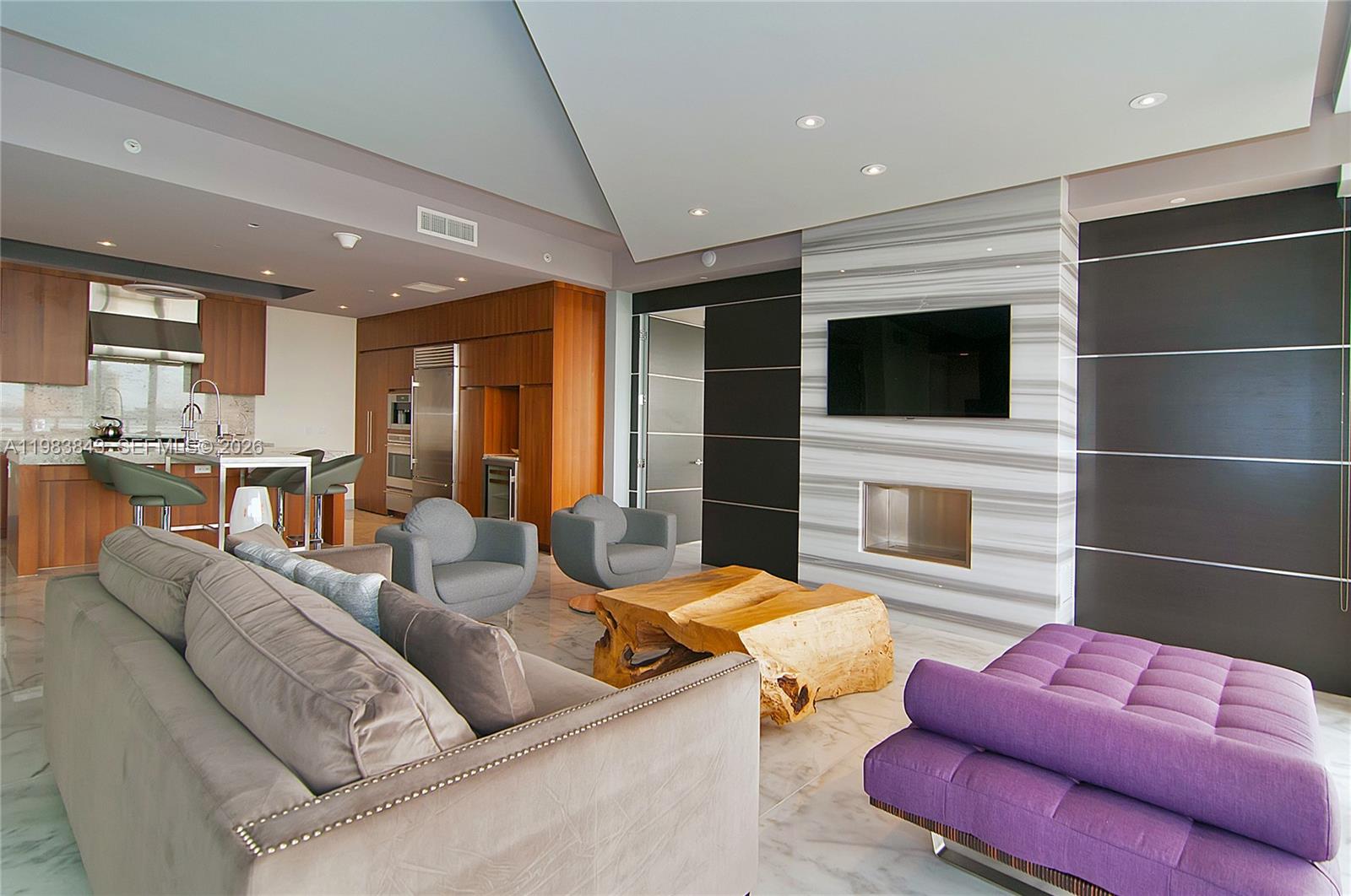 A modern living room features a marble fireplace, a wooden coffee table, and purple seating — 9705 Collins Ave # 505N, Bal Harbour FL 33154, BAL HARBOUR, FL