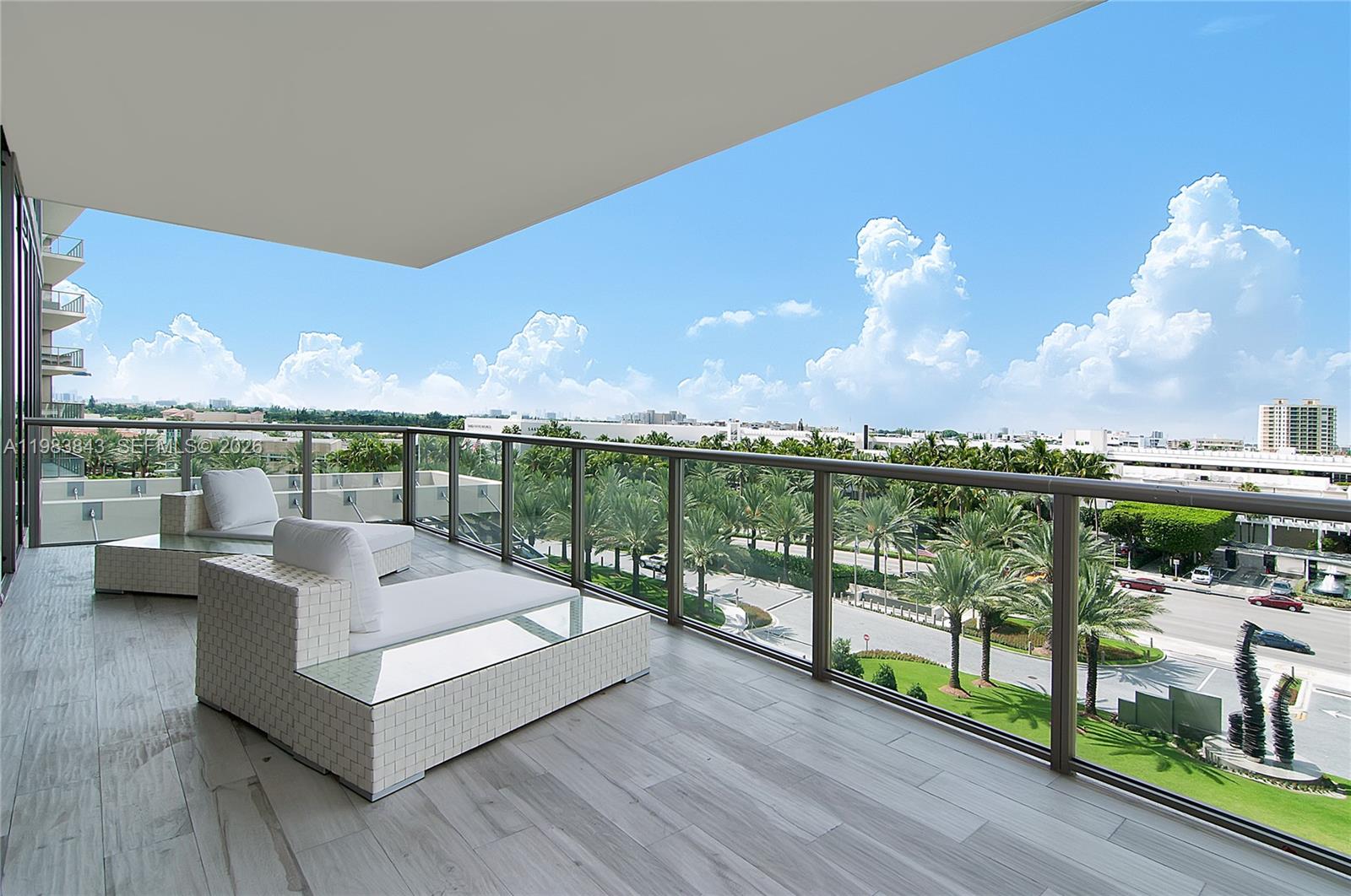 A balcony features white lounge furniture, glass railings, and a view of palm trees — 9705 Collins Ave # 505N, Bal Harbour FL 33154, BAL HARBOUR, FL