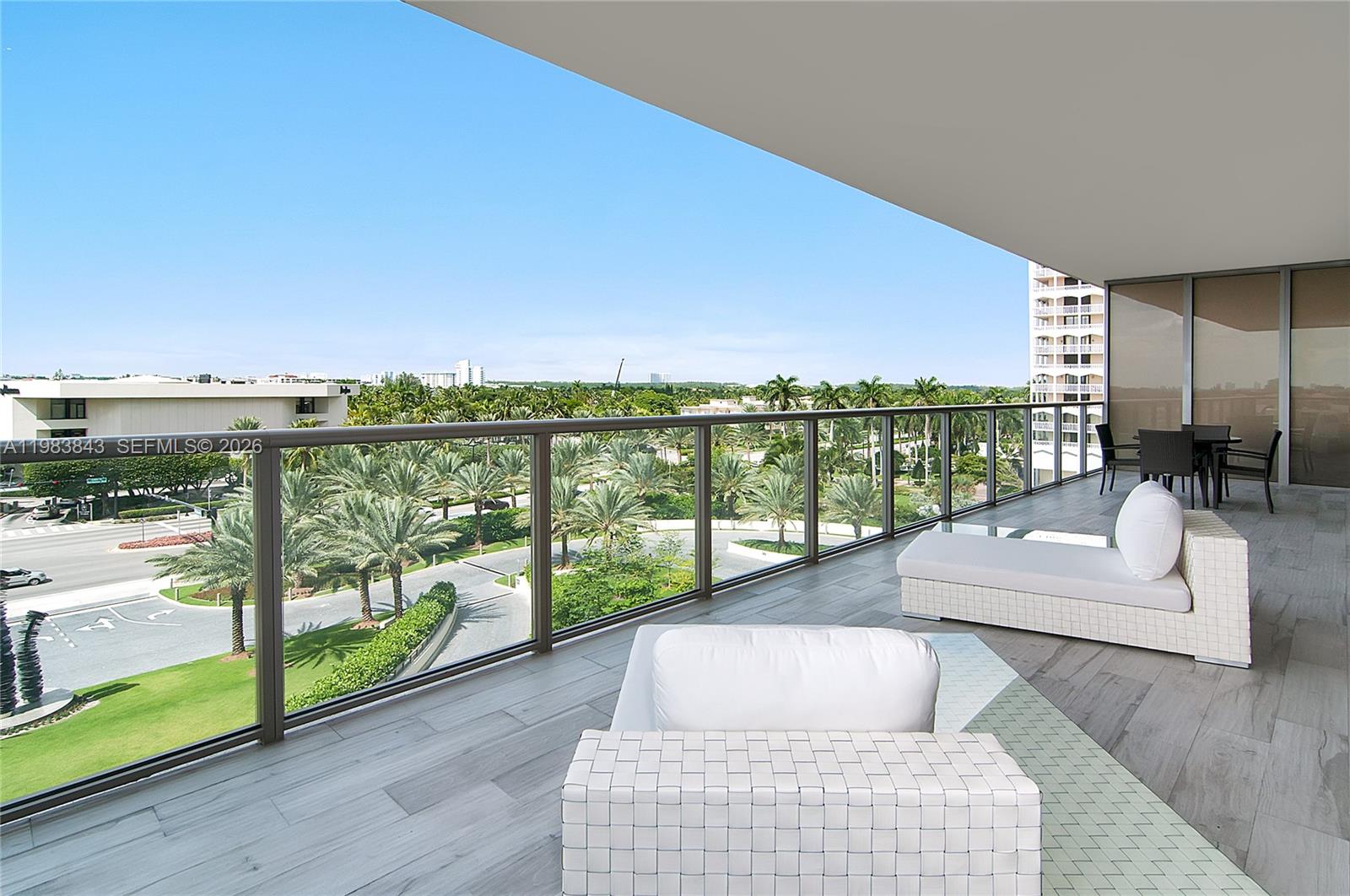 A spacious balcony features white lounge furniture, wood-look tile flooring, and a glass railing — 9705 Collins Ave # 505N, Bal Harbour FL 33154, BAL HARBOUR, FL