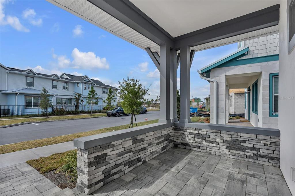 A covered front porch features stone veneer walls, gray columns, and paver flooring — 9823 PEEBLES STREET, ORLANDO, FL