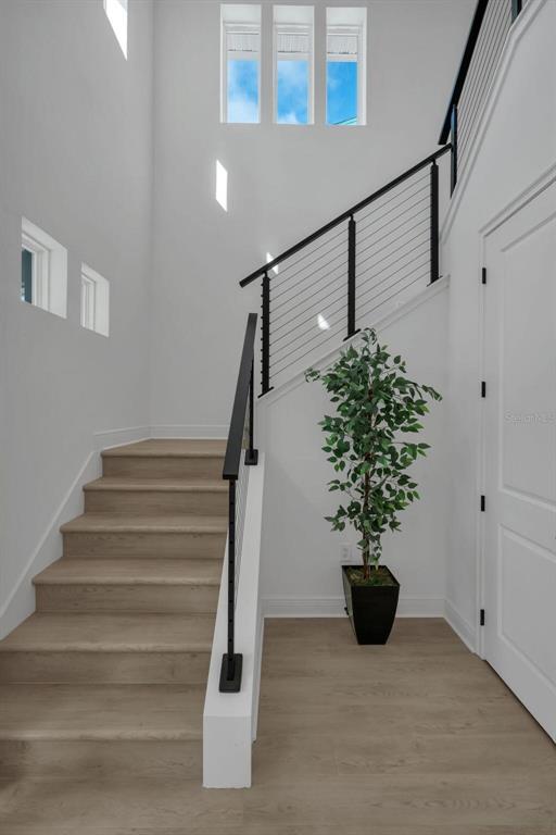 A staircase with light wood steps and a black metal railing sits in a white foyer — 9823 PEEBLES STREET, ORLANDO, FL
