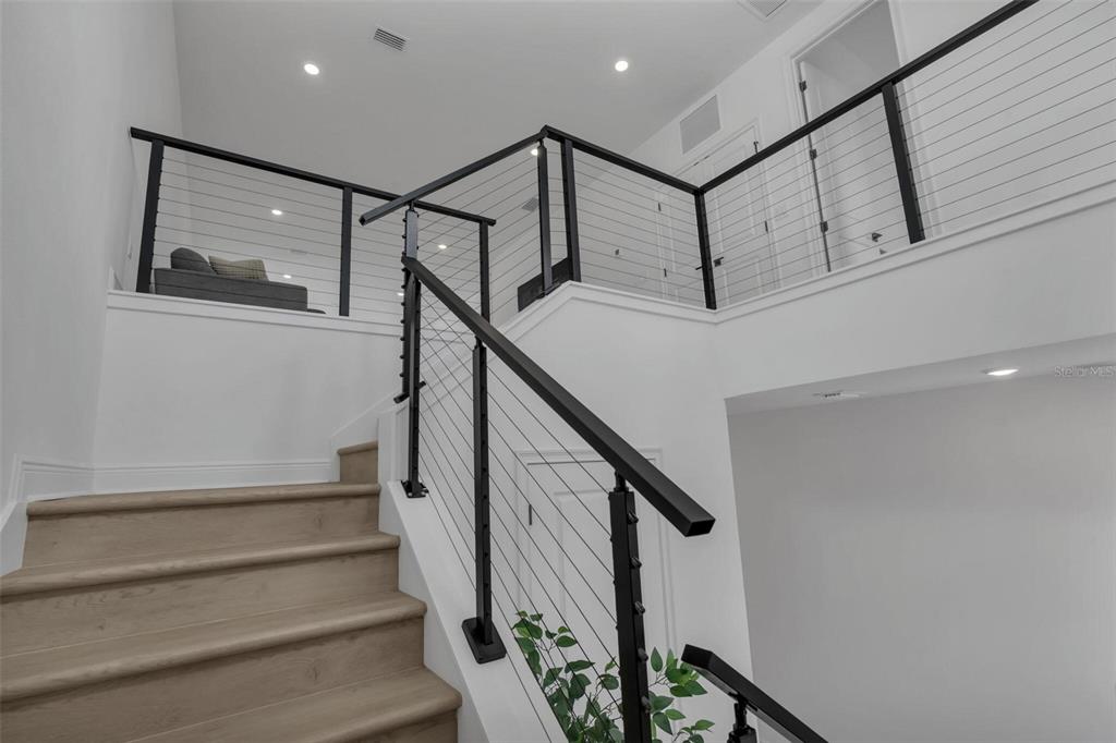 A staircase with light wood treads and a modern black metal cable railing system — 9823 PEEBLES STREET, ORLANDO, FL