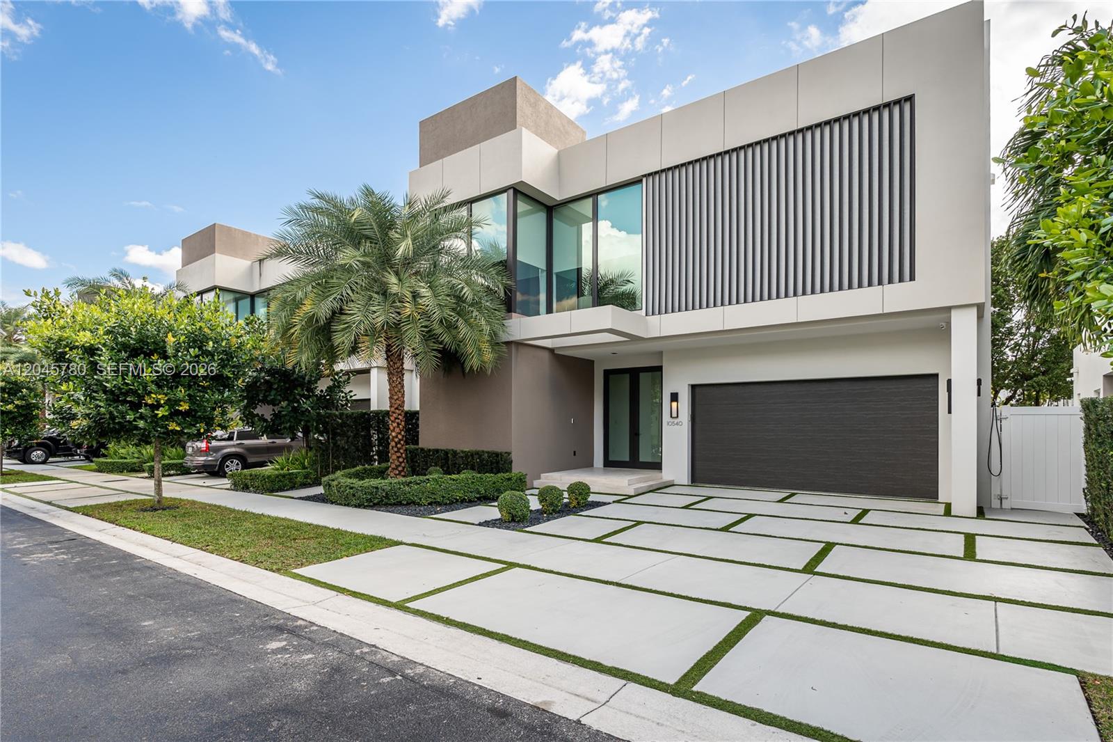 A modern two-story house features a dark garage door, large windows, and a paved driveway — 10540 NW 67th Ter, Doral FL 33178, DORAL, FL