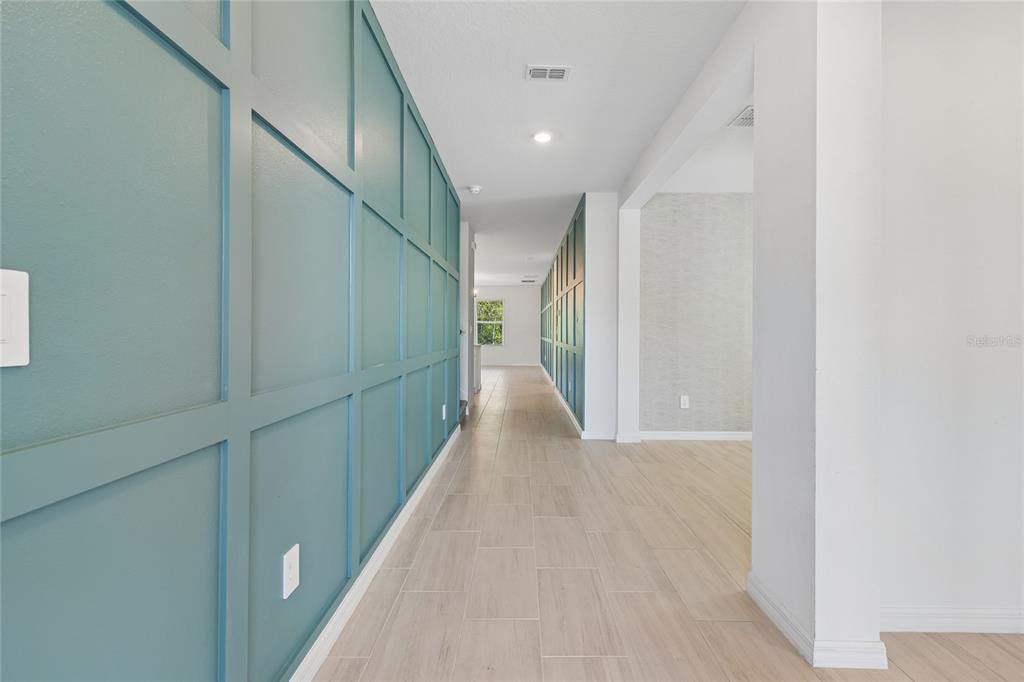 A long hallway features teal board and batten walls and light-colored wood-look tile flooring — 10065 GENTLE RAIN DRIVE, LAND O LAKES, FL