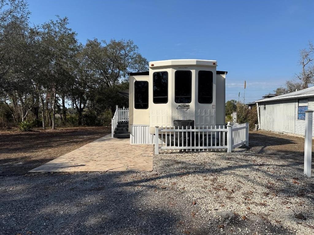 A beige park model trailer with a white picket fence and a concrete patio — 9265 GRIZZLY BEAR LANE, WEEKI WACHEE, FL