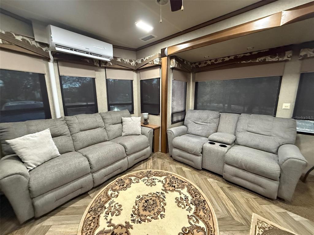A living area features two gray reclining sofas, a round patterned rug, and wall-mounted air conditioning — 9265 GRIZZLY BEAR LANE, WEEKI WACHEE, FL
