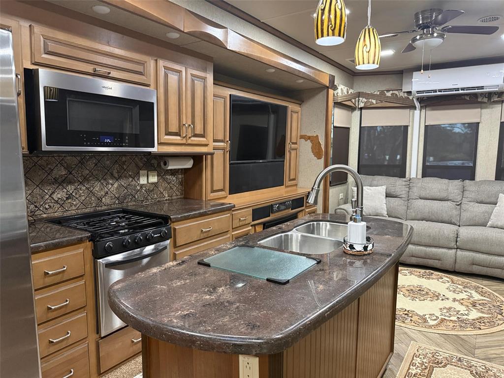 A kitchen island with a double sink sits before wooden cabinets, appliances, and a sofa — 9265 GRIZZLY BEAR LANE, WEEKI WACHEE, FL