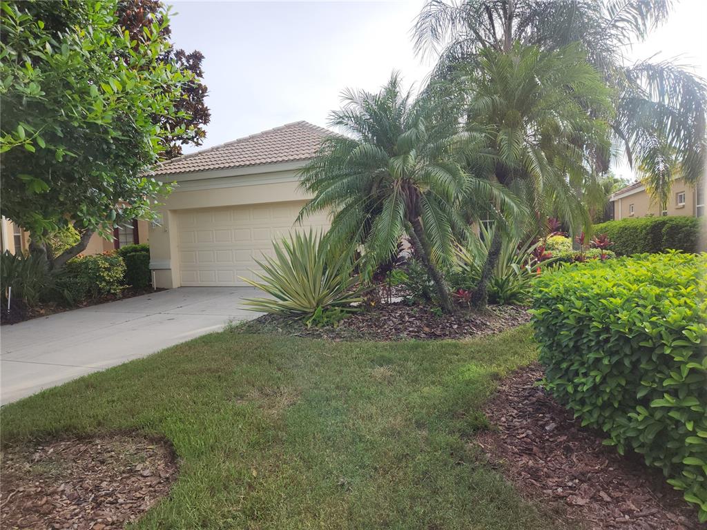 A beige house exterior features a garage, a concrete driveway, and tropical landscaping — 6642 TAILFEATHER WAY, BRADENTON, FL