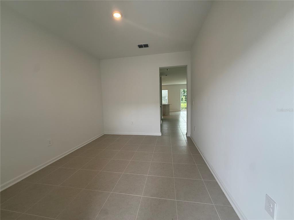 An empty room with light-colored tile flooring and white walls leads to a hallway — 3061 CHROMATIC STREET, KISSIMMEE, FL