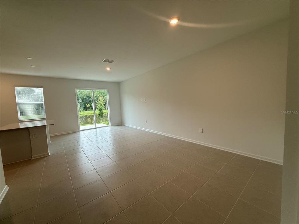 An open-concept living area features light-colored tile flooring, a sliding glass door, and recessed lighting — 3061 CHROMATIC STREET, KISSIMMEE, FL