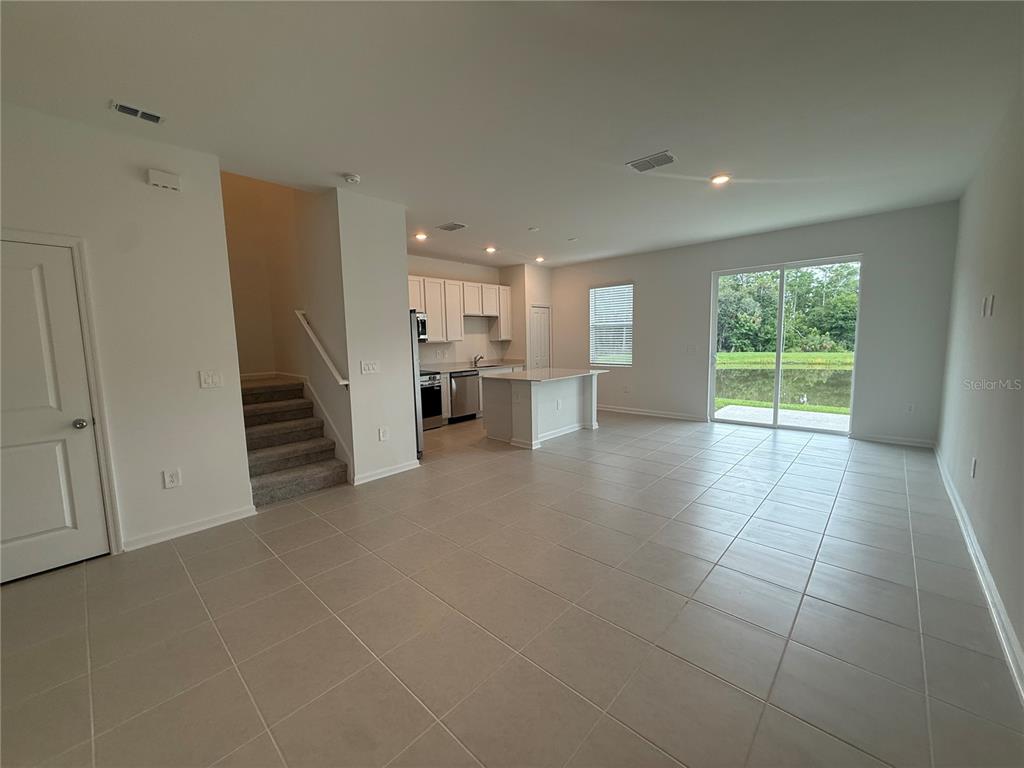 An open-concept living area features tile flooring, a kitchen with white cabinets, and sliding doors — 3061 CHROMATIC STREET, KISSIMMEE, FL