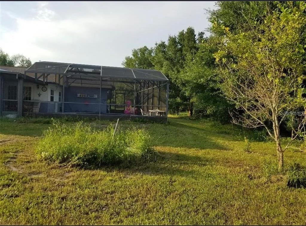 A screened-in patio attached to the back of a house sits on a grassy lot — 3050 CHINA BERRY COURT, KISSIMMEE, FL