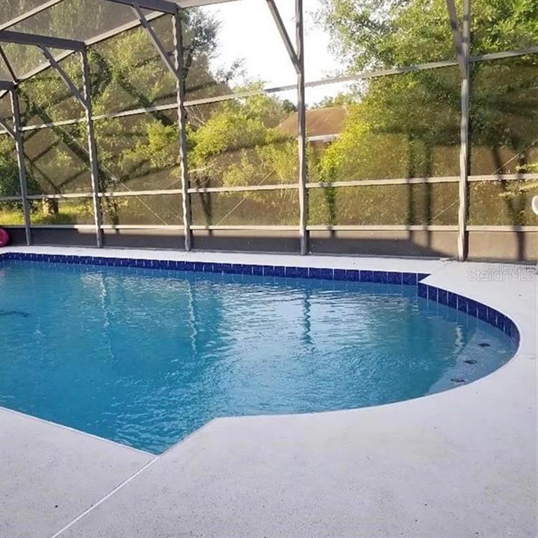 A swimming pool with blue tile trim is enclosed by a screened-in lanai — 3050 CHINA BERRY COURT, KISSIMMEE, FL