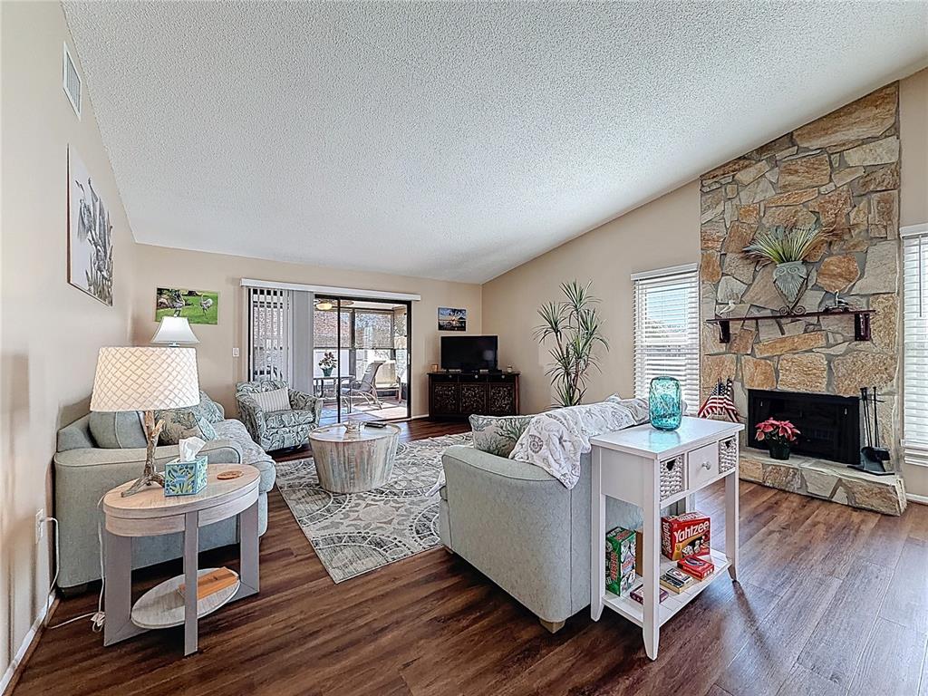 A living room features a stone fireplace, wood-look flooring, and a sliding glass door — 9961 EAGLES POINT CIRCLE UNIT 4, PORT RICHEY, FL