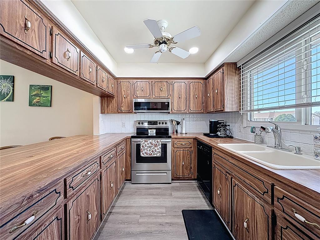 A galley kitchen features wood-grain cabinets, stainless steel appliances, and a white tiled backsplash — 9961 EAGLES POINT CIRCLE UNIT 4, PORT RICHEY, FL