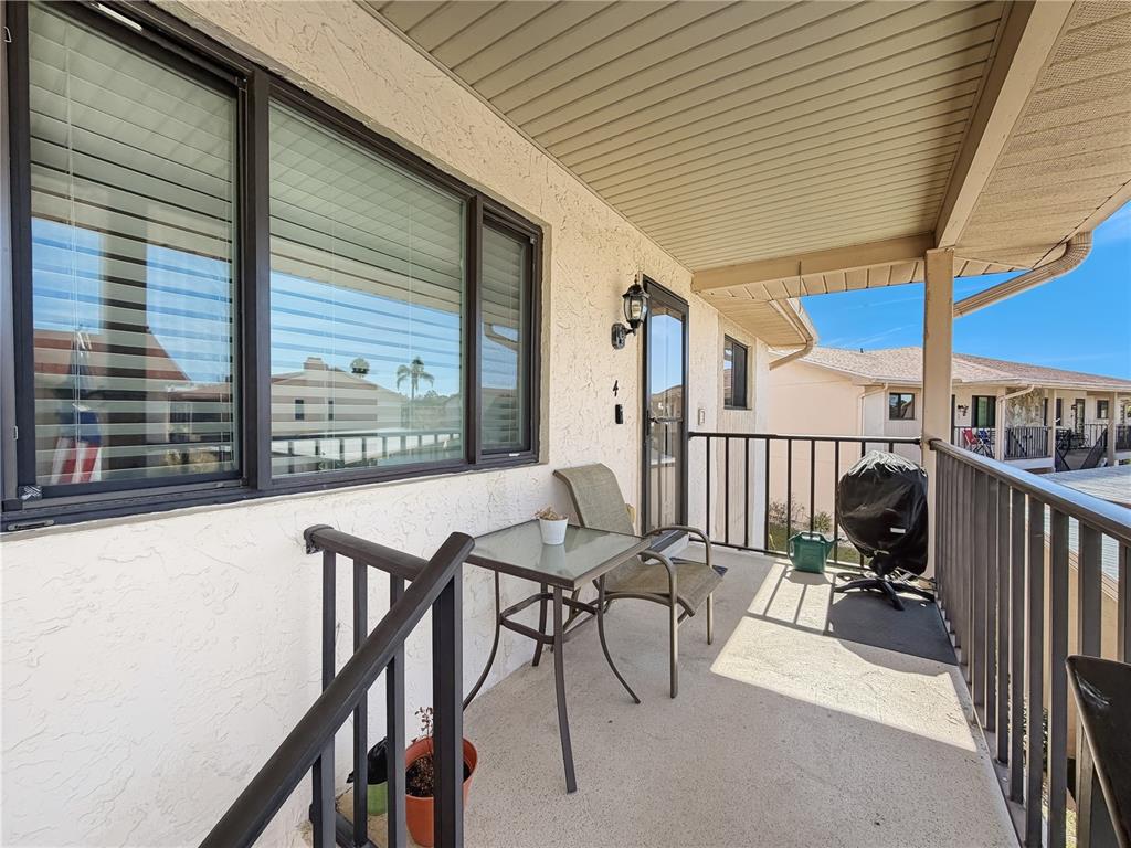 A covered balcony features a small glass table, a chair, and a black grill — 9961 EAGLES POINT CIRCLE UNIT 4, PORT RICHEY, FL