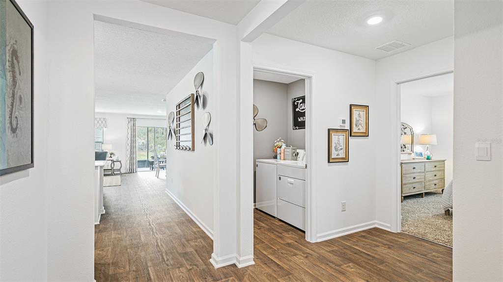 A hallway with wood-look flooring leads to a laundry room and a bedroom — 89 BEAVERDAM LANE, PALM COAST, FL