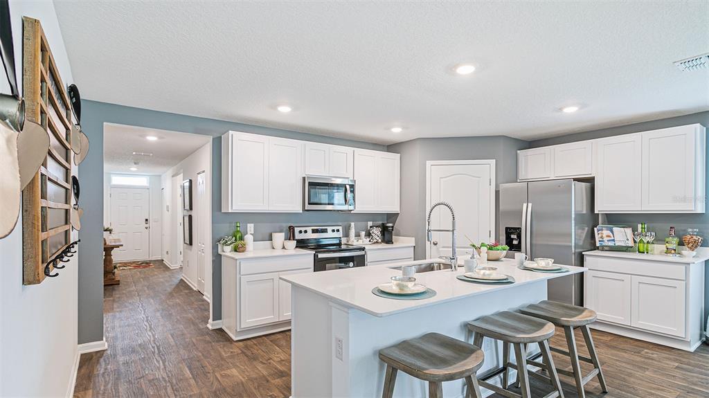 A kitchen features white cabinets, stainless steel appliances, a center island, and wood-look flooring — 89 BEAVERDAM LANE, PALM COAST, FL