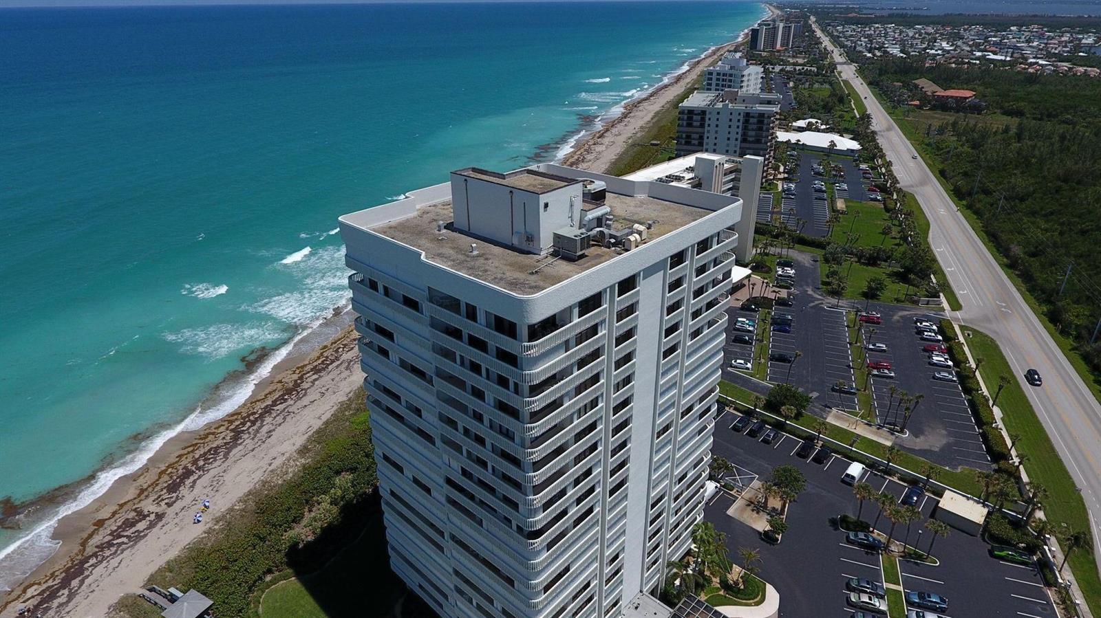 An aerial view shows a tall beachfront condominium building next to a parking lot and road — 9960 S Ocean Drive # 1402, Jensen Beach FL 34957, JENSEN BEACH, FL