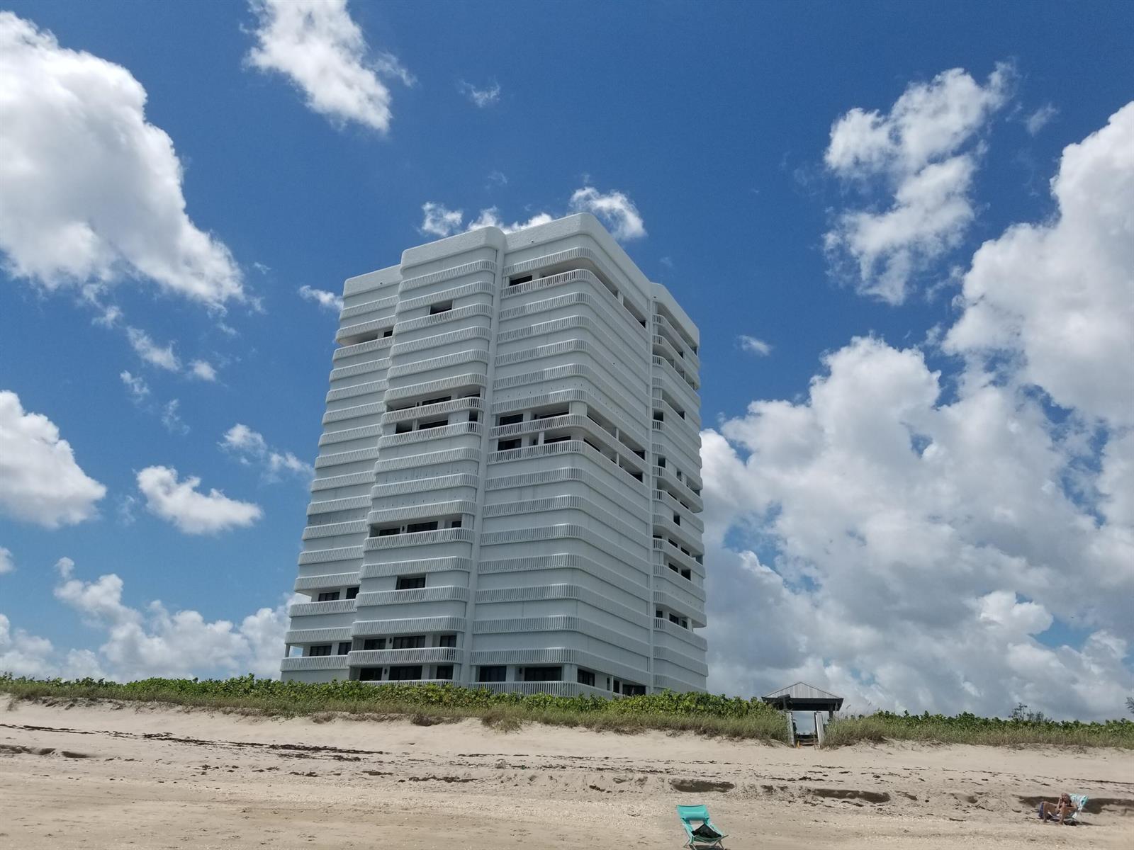 A tall, white, multi-story residential building stands behind a sandy beach under a blue sky — 9960 S Ocean Drive # 1402, Jensen Beach FL 34957, JENSEN BEACH, FL