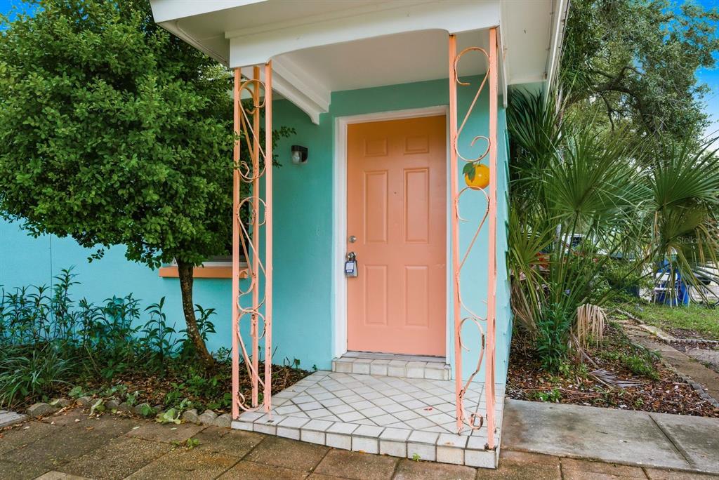 A light blue exterior wall features a peach-colored front door framed by decorative metal posts — 417 MILWAUKEE AVENUE, DUNEDIN, FL